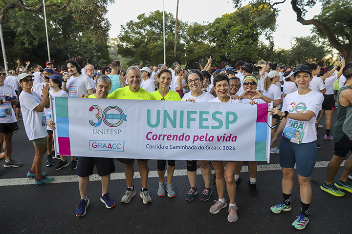 Membros da equipe da Unifesp e da Nicorunners, equipe de corredores(as) formada por alunos(as), professores(as), funcionários(as)e egressos(as) da Escola Paulista de Medicina, que participam de maratonas de Revezamento, segurando a faixa comemorativa dos 30 anos da Unifesp