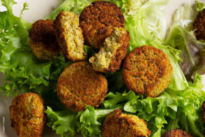 Imagem do que parece ser falafel, um prato popular do Oriente Médio, normalmente feito de grão de bico moído ou favas, temperos e ervas e depois frito até obter uma textura crocante. Muitas vezes são servidos em uma cama de verduras, em pão pita ou com molhos como tahine ou homus.